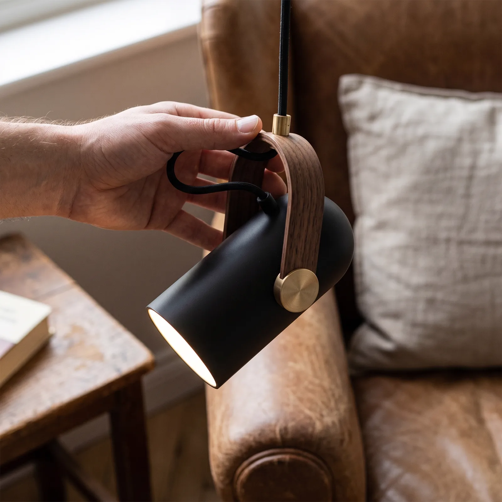 The pendant lamp's matte-black body, walnut-grain strap and brushed-brass pivot disc